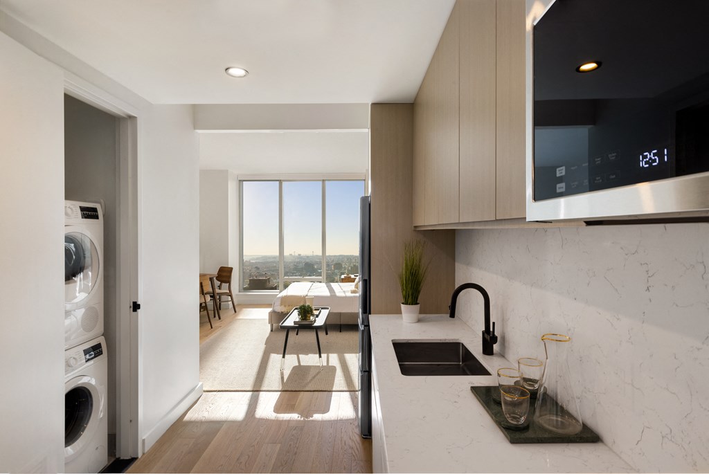 a kitchen with a sink and a dishwasher and a living room with a window at The Paxton, Brooklyn, NY 11201